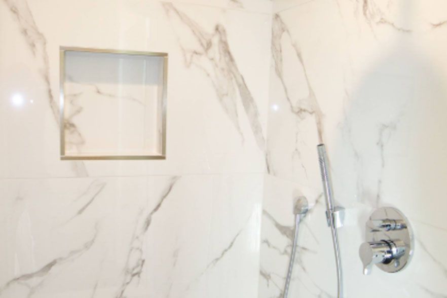 Marble-tiled shower wall with a built-in niche and chrome shower control.