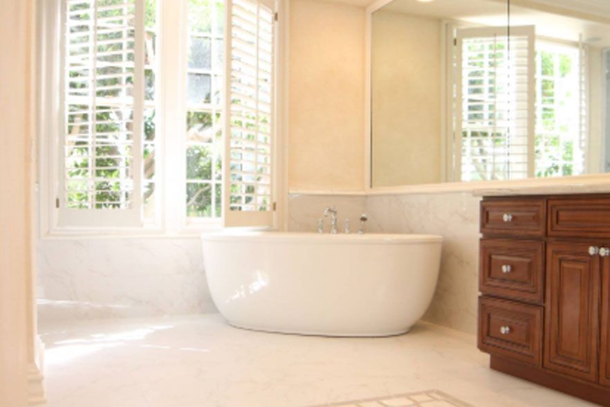Bright bathroom with a freestanding tub, white tile, and a wooden vanity by sunlit windows.