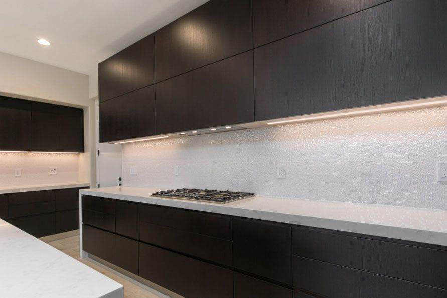 Modern kitchen with dark cabinets, white countertops, and a stainless steel cooktop