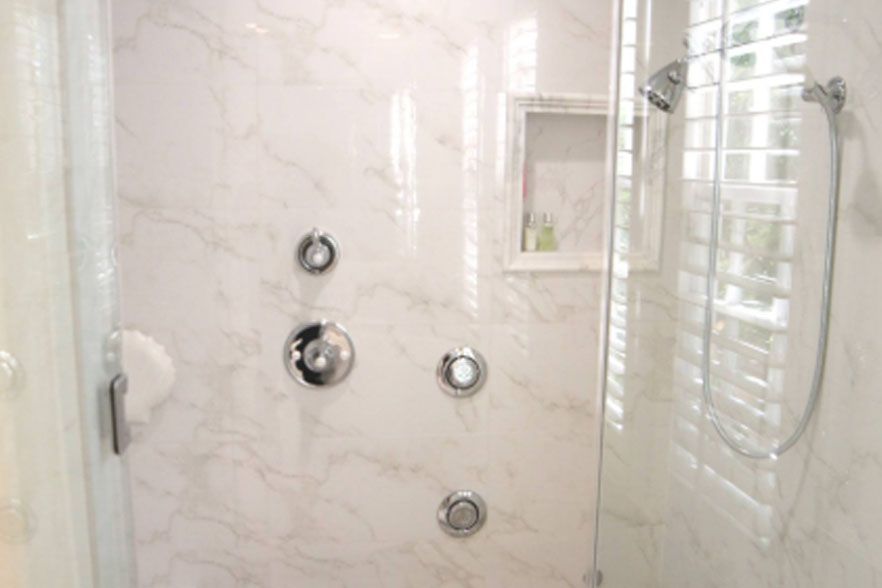 White marble-tiled bathroom shower with chrome fixtures and a window with white blinds