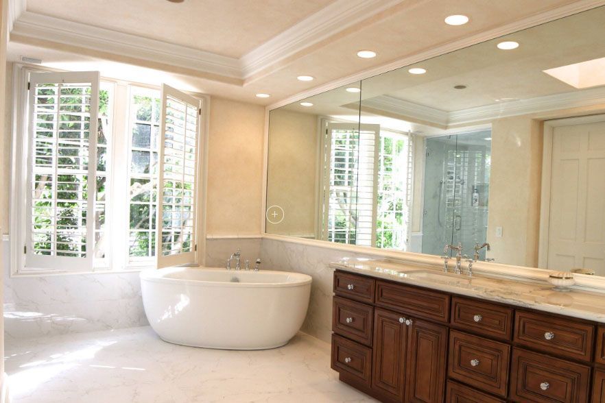 Bright bathroom with a freestanding tub, double vanity, large mirror, and white plantation shutters