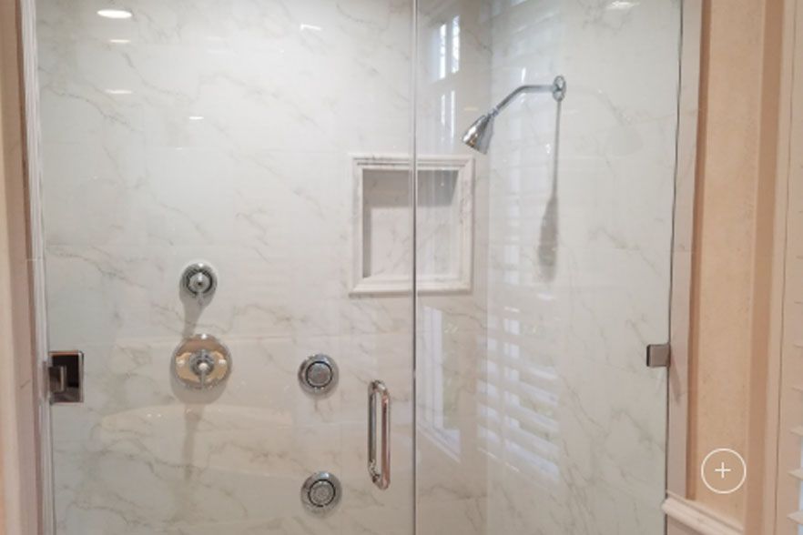 Glass shower enclosure with marble-tile walls, built-in shelf, and chrome shower fixtures
