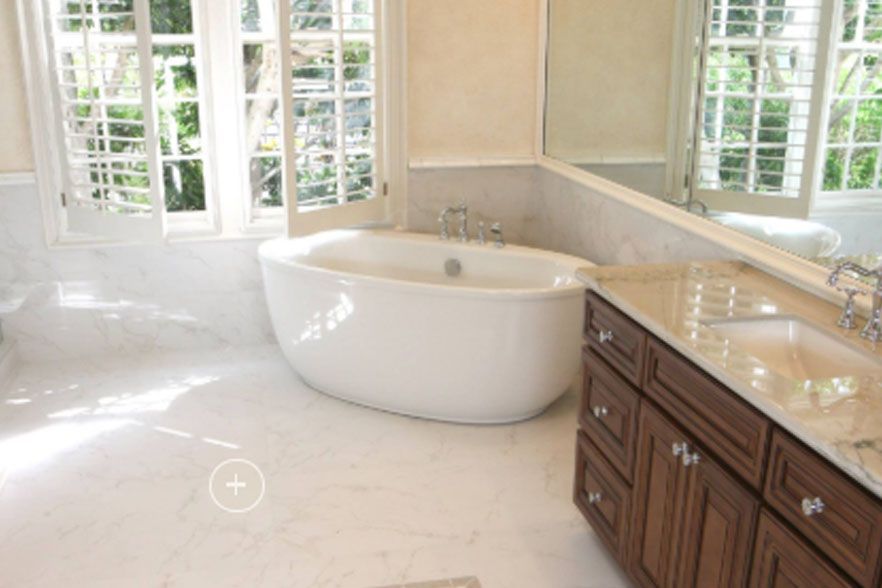 Bright bathroom with a freestanding tub, marble floor, and wooden vanity by large windows