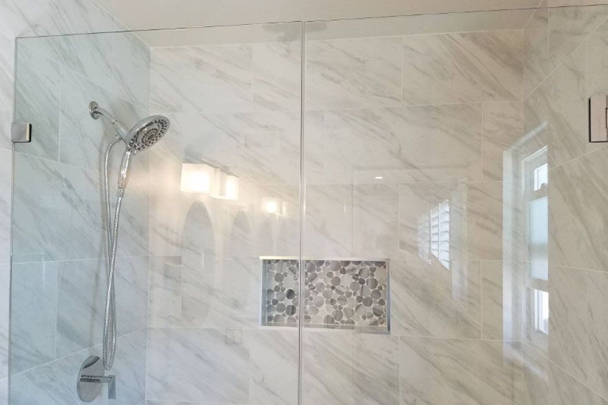 Glass walk-in shower with marble tile, wall-mounted showerhead, and built-in niche.