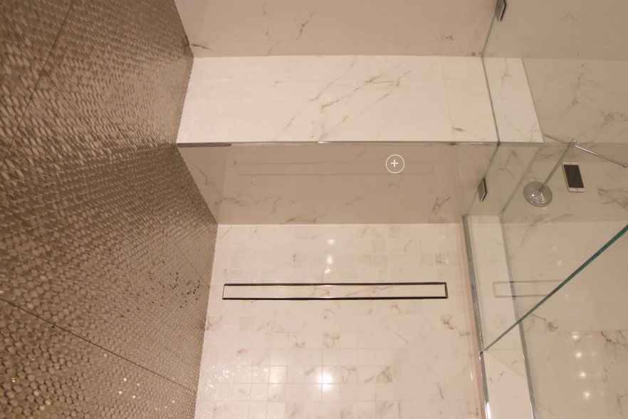 Top-down view of a tiled floor, wall, and glass shower enclosure with a narrow floor drain.