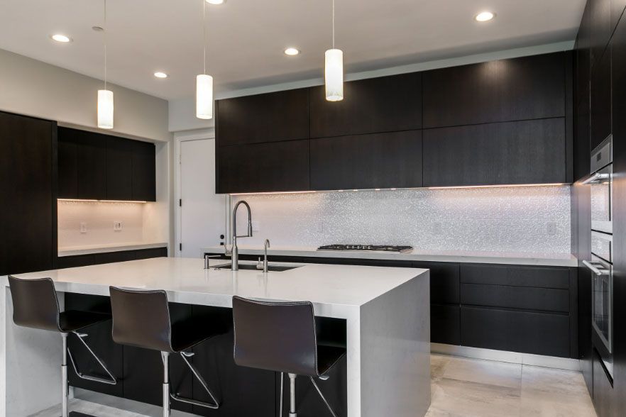 Modern black-and-white kitchen with island, bar stools, pendant lights, and sleek cabinetry