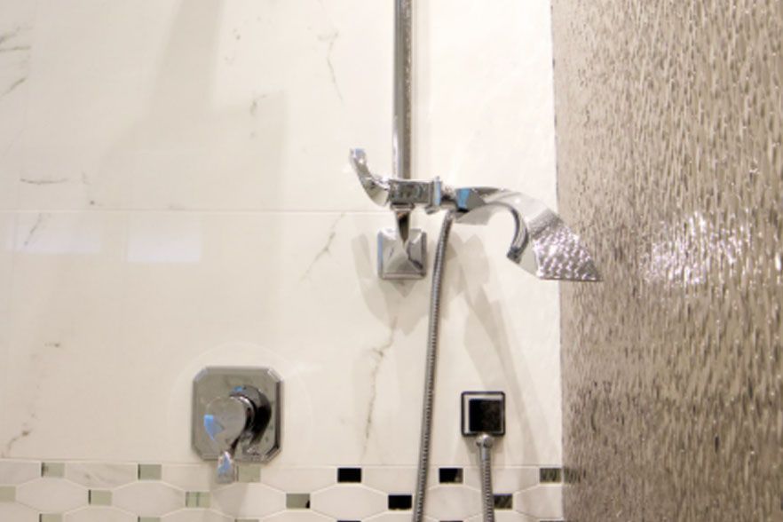 Shower stall with chrome showerhead, faucet, and tiled bathroom wall