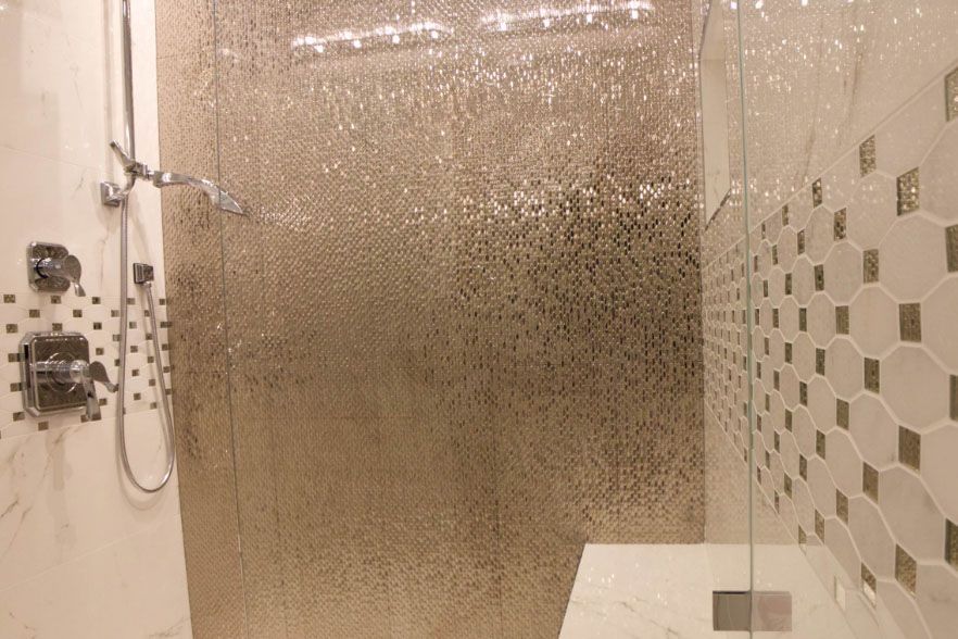 Modern shower with glass enclosure, beige tile walls, and shower fixtures on the left