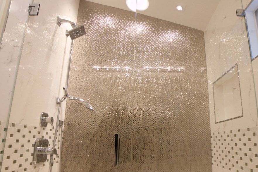 Glass shower enclosure with pebble mosaic tile wall and shower fixtures in a bathroom