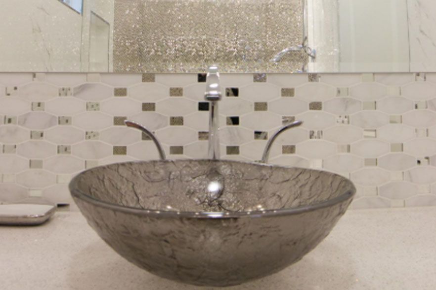 Modern bathroom sink with a clear glass basin, chrome faucet, and mosaic tile backsplash.