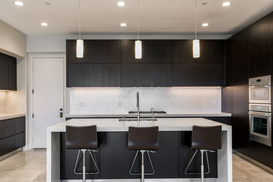 Modern kitchen with dark cabinets, white island, pendant lights, and three bar stools
