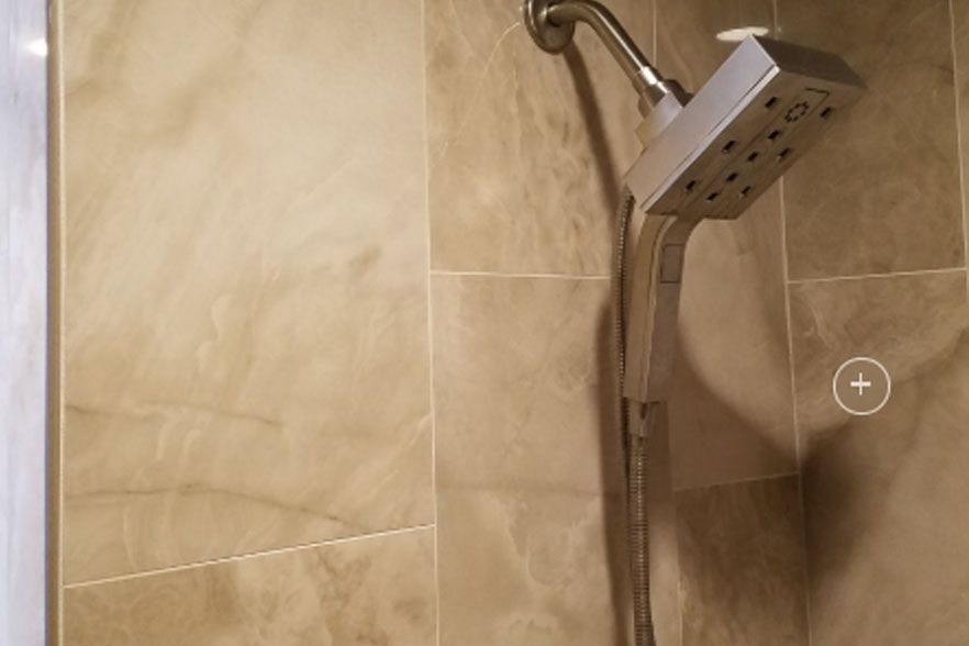 Bathroom shower with chrome handheld showerhead and beige tiled wall.