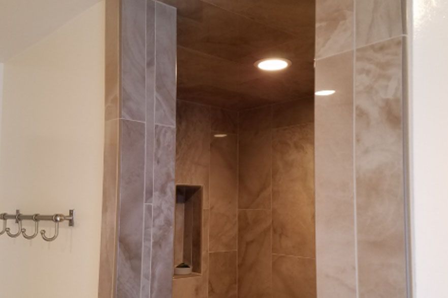 Tiled shower stall with beige walls, recessed light, and a built-in shelf
