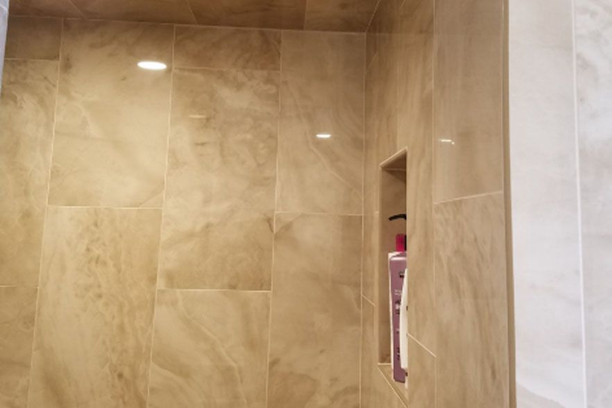 Beige tiled shower wall with recessed niche holding toiletries