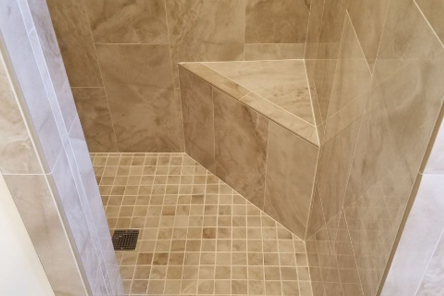 Walk-in shower with beige tile, small mosaic floor, corner bench, and drain.