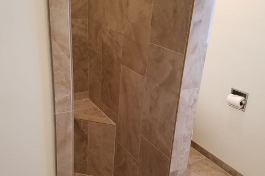 Tiled shower stall with brown stone walls and a small recessed shelf, next to a toilet paper holder