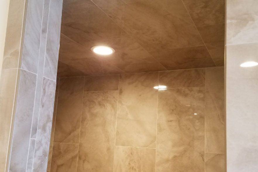 Tiled shower stall with beige walls and a recessed ceiling light