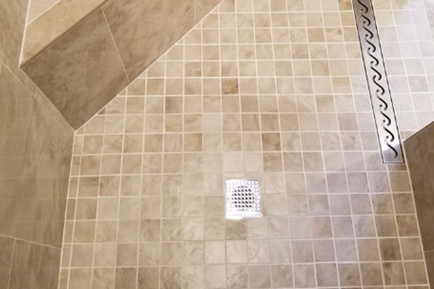 Tiled shower floor with a white drain cover and beige walls.
