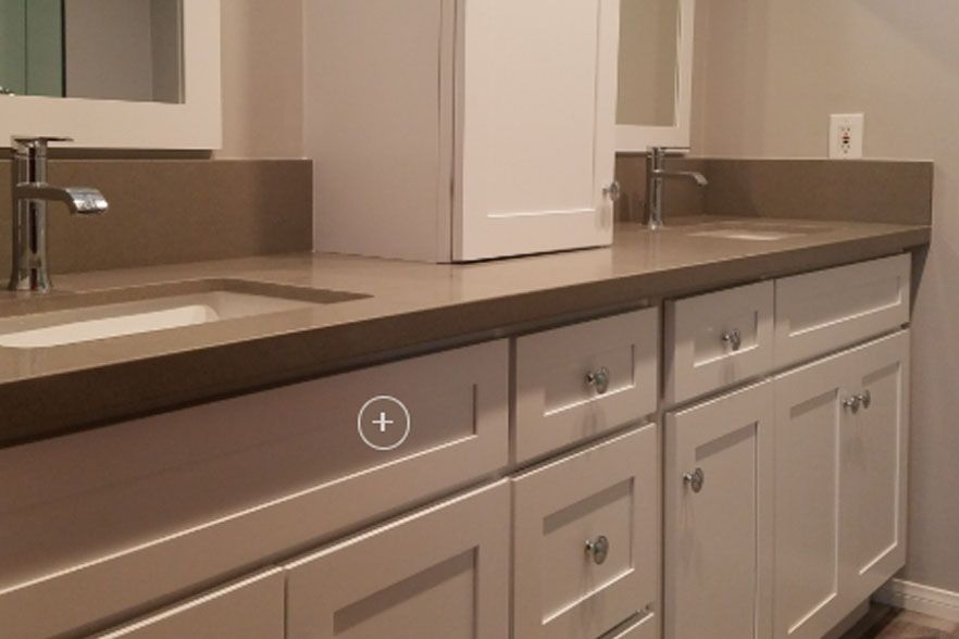 Modern kitchen with beige cabinets, dark countertops, double sink, and a refrigerator in the background