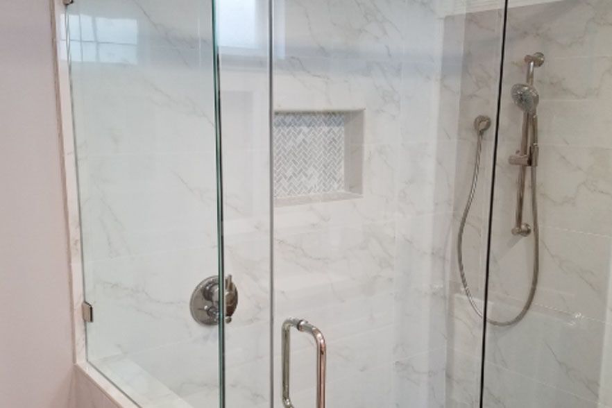 Glass shower enclosure with chrome fixtures and white tiled walls
