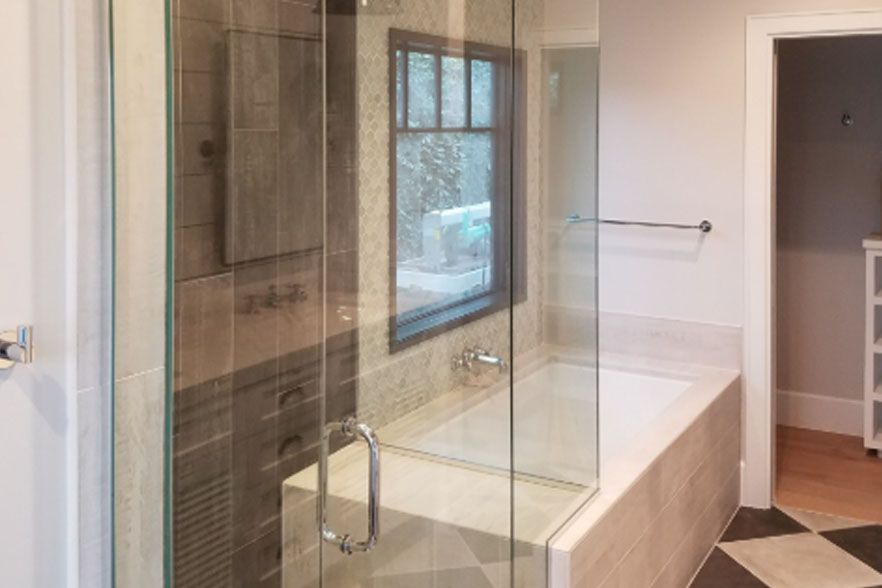 Modern bathroom with glass-enclosed bathtub, tiled shower, towel rack, and open doorway to another room