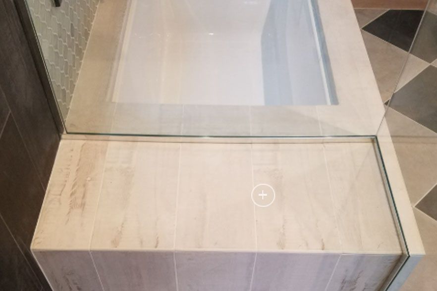 Small step into a glass shower enclosure with a beige tiled ledge and floor.