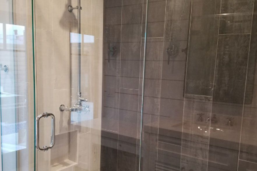 Glass shower enclosure with chrome handles and dark tiled walls in a bathroom