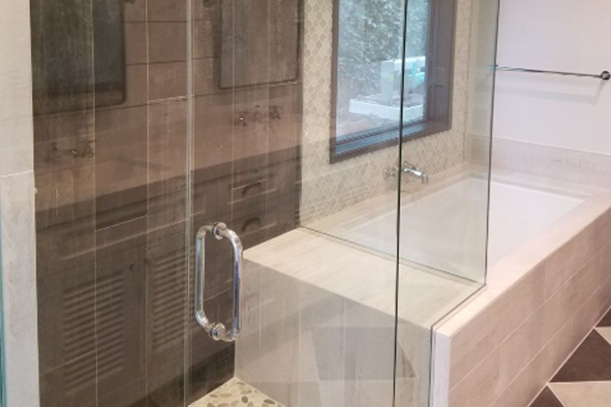 Modern bathroom with glass shower enclosure, tiled walls, and a bathtub beside a window