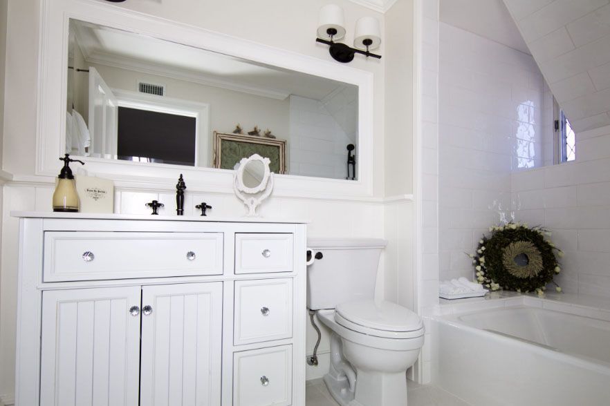 White bathroom with vanity, mirror, toilet, and bathtub under a slanted ceiling
