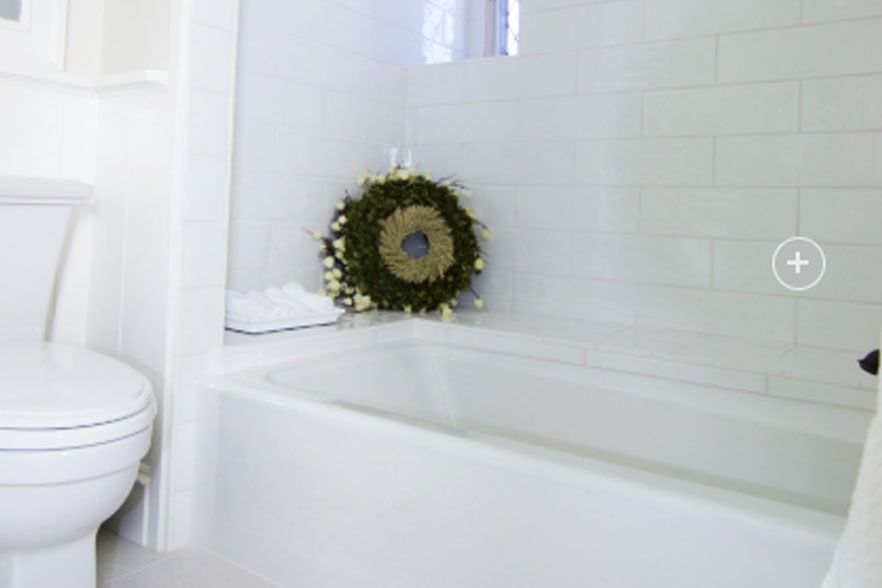 White bathroom with a tub, toilet, and wreath hanging on the wall.