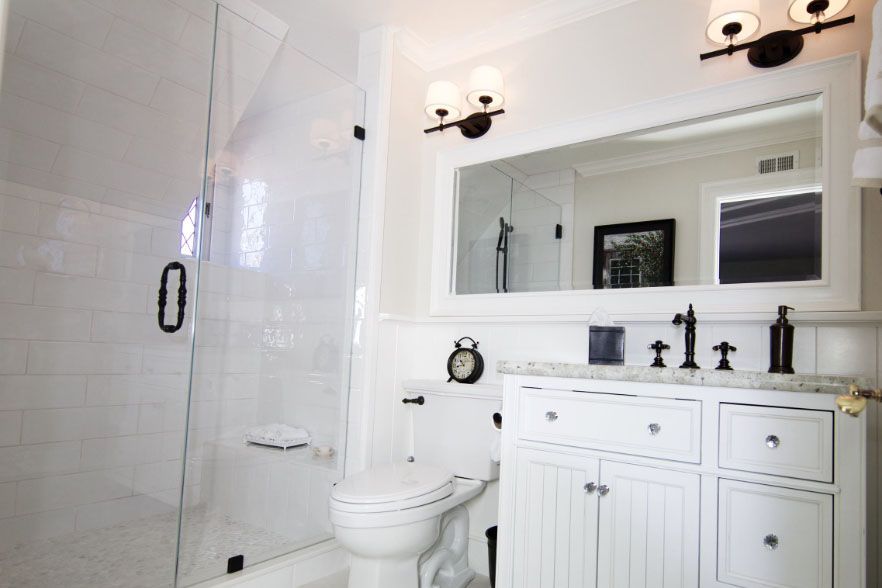 Bright white bathroom with glass shower, toilet, vanity sink, and large mirror.