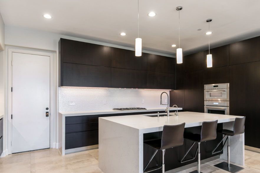 Modern minimalist kitchen with dark cabinets, white island, pendant lights, and three bar stools
