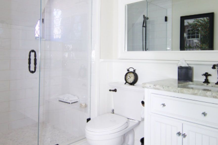 White bathroom with toilet, vanity sink, large mirror, and glass shower door
