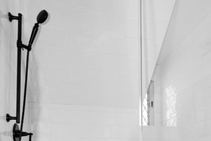 Black shower fixture against white tiled shower wall with a glass partition