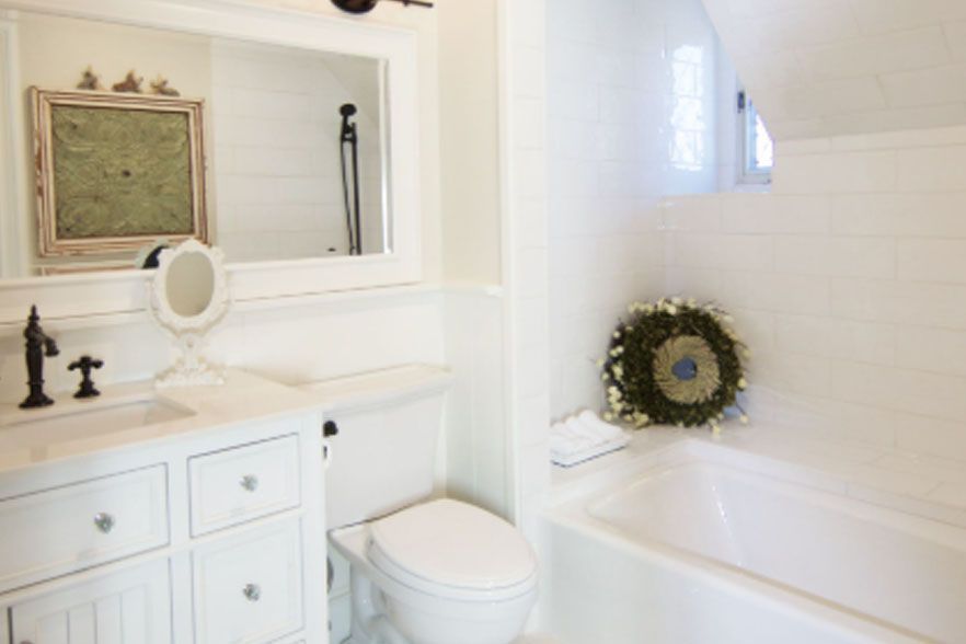 Bright white bathroom with vanity, toilet, bathtub, and a wreath on the tub ledge