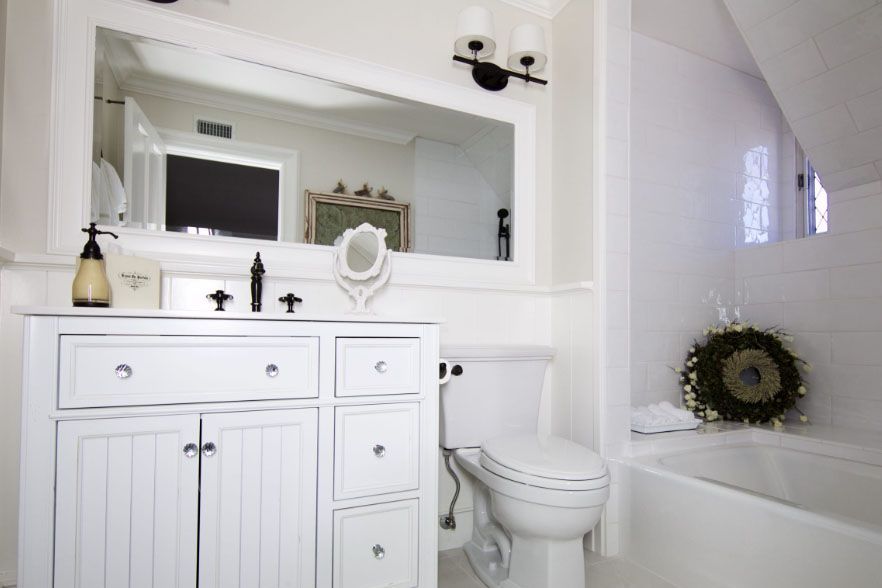 Bright white bathroom with vanity, mirror, toilet, and bathtub with a wreath on the edge