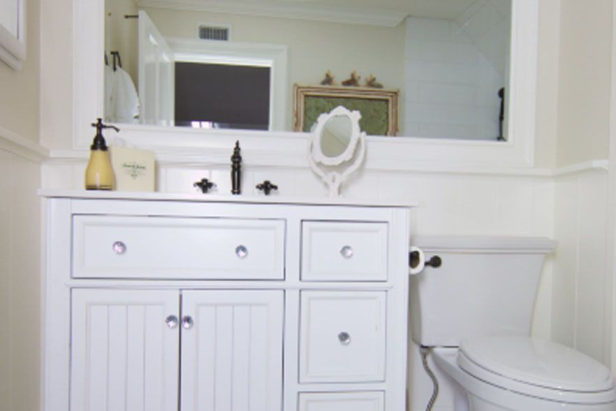 White bathroom vanity with sink, mirror, and toilet in a bright, clean room