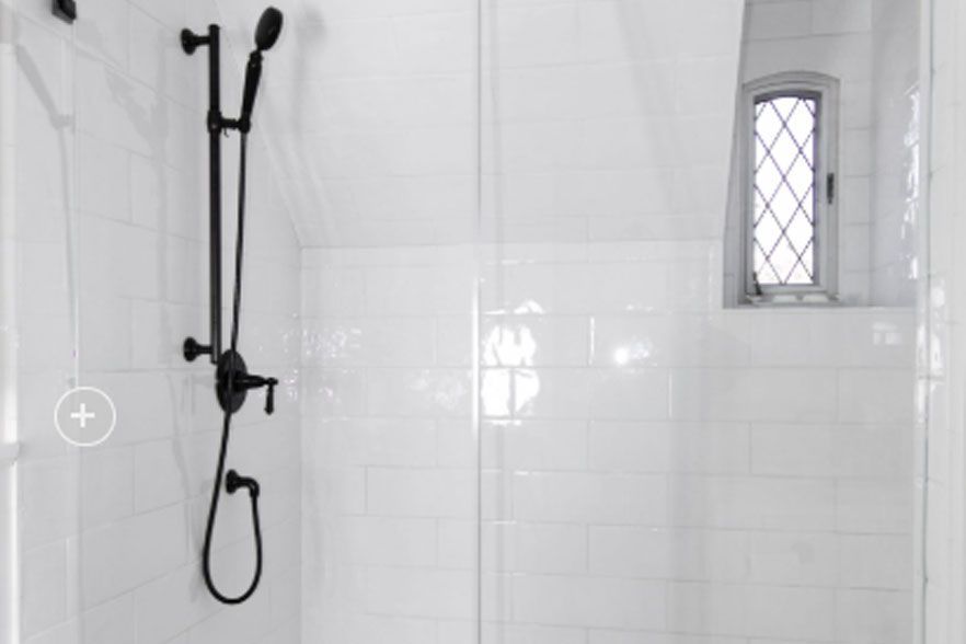 White tiled shower with a black handheld showerhead and a small frosted window.