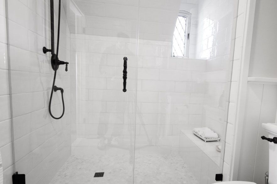 White tiled shower with black fixtures, glass door, and a small window.