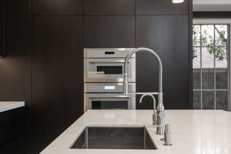 Modern kitchen with dark cabinetry, white island countertop, and built-in oven and microwave.