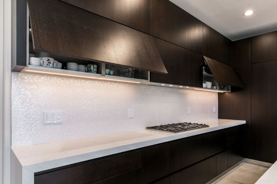 Modern kitchen with dark wood cabinets, white countertop, built-in gas cooktop, and under-cabinet lighting.