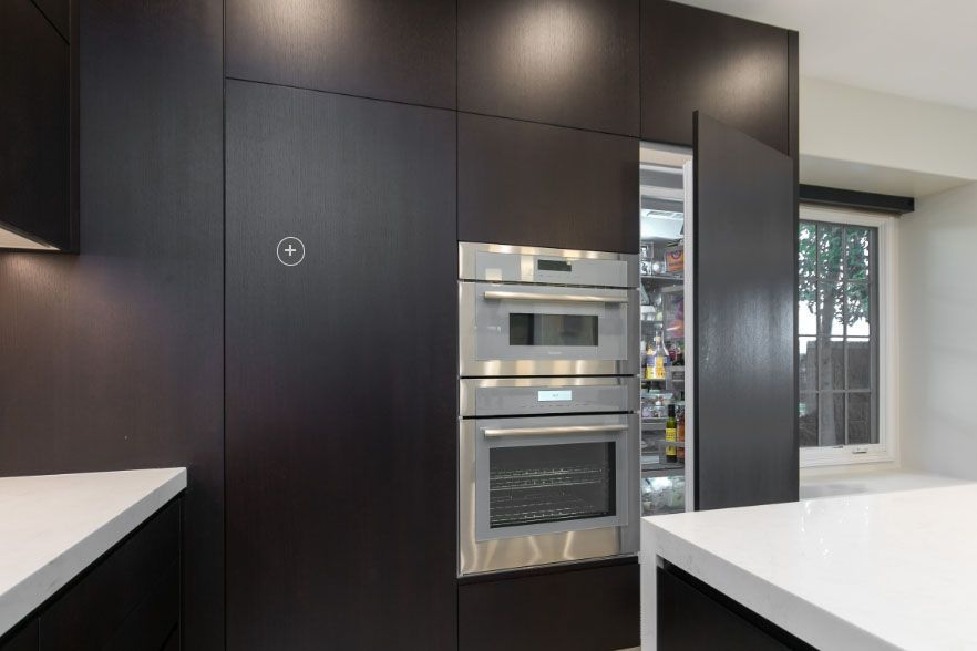 Modern kitchen with dark cabinets, built-in stainless steel oven, and white countertops