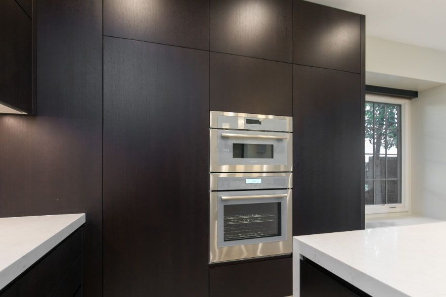 Modern kitchen with dark cabinets, built-in stainless steel oven, and white countertops