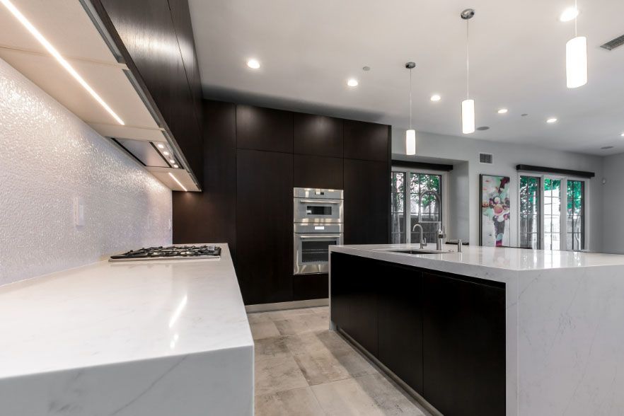 Modern kitchen with white countertops, black island, built-in oven, and large windows
