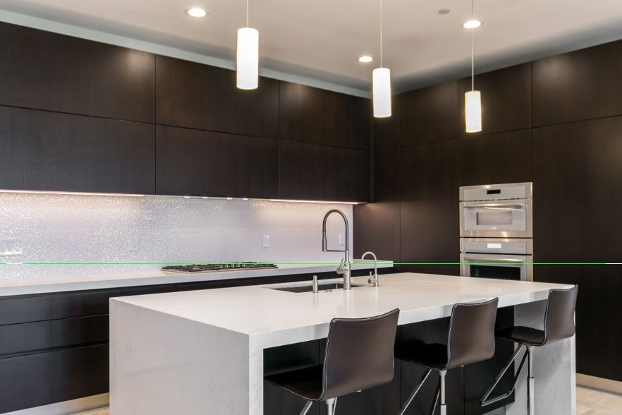 Modern kitchen with dark cabinets, white island, pendant lights, and three bar stools