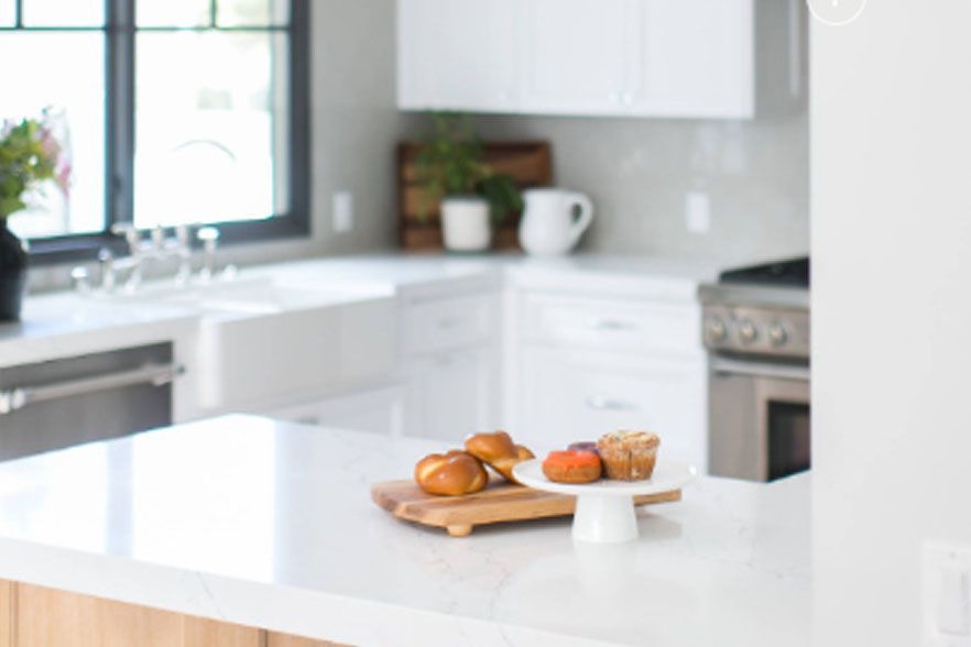 Bright kitchen with a white island, pastries on a wooden board, and a stove in the background