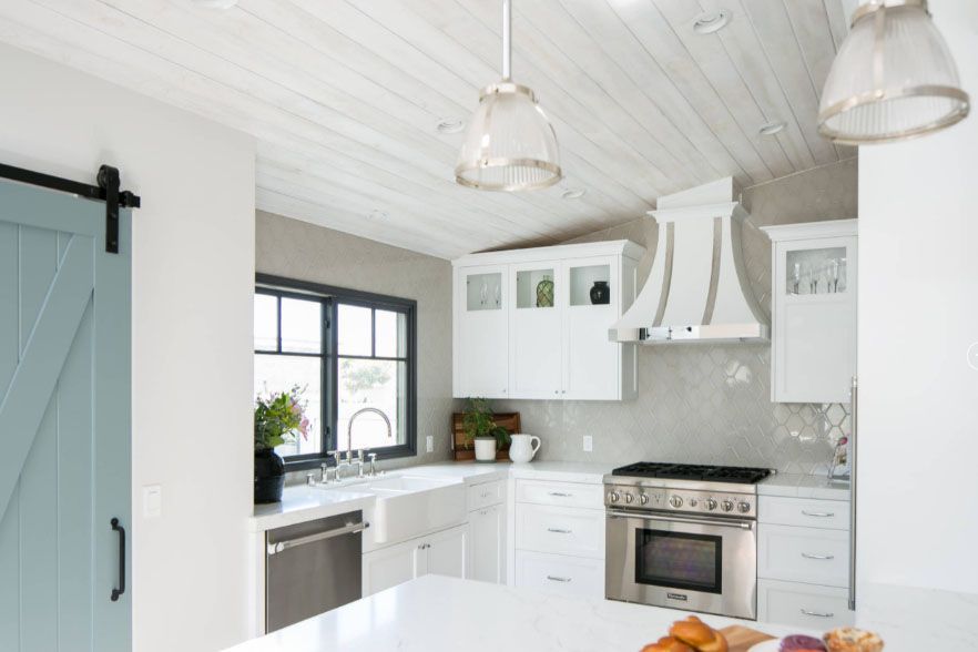Bright white modern kitchen with gray accents, stove, sink, and window under hanging lights