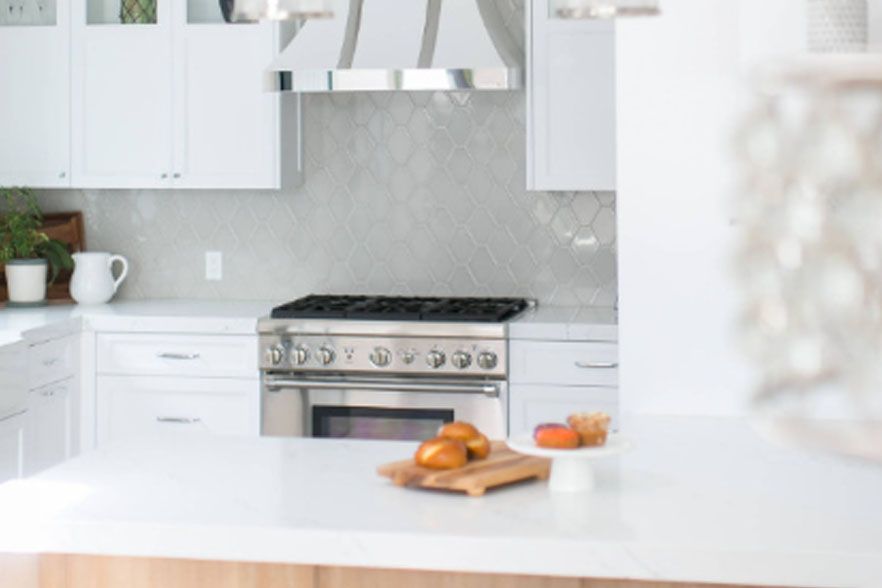 Bright white kitchen with stainless steel stove and a bowl of oranges on the counter