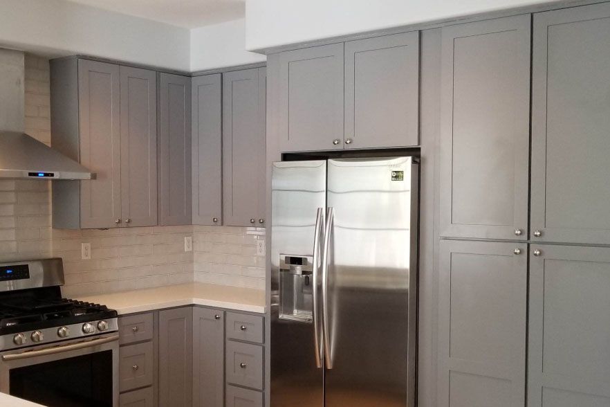 Modern kitchen with gray cabinets, stainless steel refrigerator, stove, and white tile backsplash