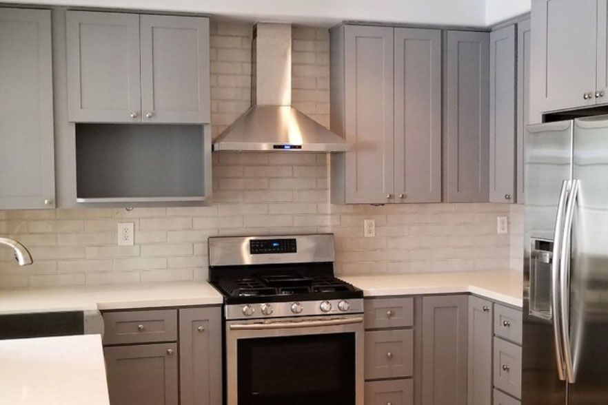Modern kitchen with gray cabinets, stainless steel appliances, and white tile backsplash